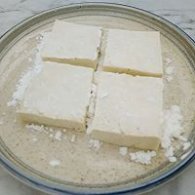 步骤图:淀粉倒入平盘中，把豆腐两面均匀粘上淀粉。
